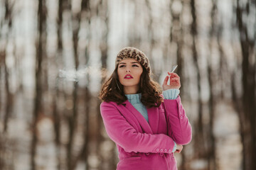 Poster - Young Caucasian female wearing a pink coat and smoking in a park with trees in the backgroun