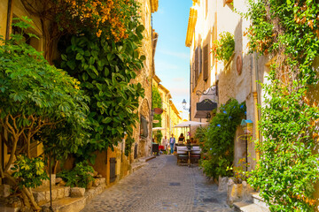 Wall Mural - A picturesque back street with tourists enjoying a sidewalk cafe in the medieval hilltop village of Saint-Paul de Vence in the Provence Cote d'Azur region of Southern France.