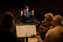 Conductor Of Symphony Orchestra With Performers In Background In Concert Hall