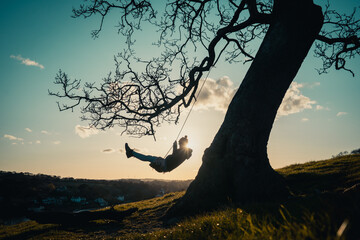 Silhouette of a female enjoying the sunset on a tree swing in a mountainous area