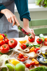 Beautiful young woman slicing red ripe tomato, preparing delicious fresh vitamin salad. Concept of clean eating, healthy food, low calories meal, dieting, self caring lifestyle. Close up