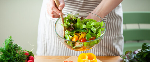 Wall Mural - Beautiful young woman preparing delicious fresh vitamin salad. Concept of clean eating, healthy food, low calories meal, dieting, self caring lifestyle. Colorful vegetables, glass bowl. Banner