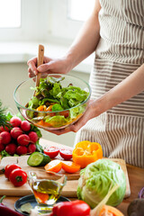 Wall Mural - Beautiful young woman preparing delicious fresh vitamin salad. Concept of clean eating, healthy food, low calories meal, dieting, self caring lifestyle. Colorful vegetables, glass bowl. Close up