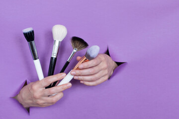 professional makeup brushes in your hands, on a purple background, holes in the background. Space for text