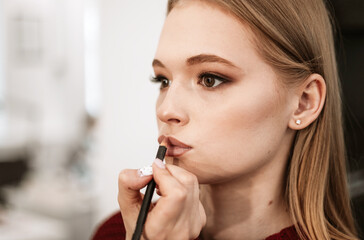 Wall Mural - makeup artist paints lips with lipstick with a brush on a beautiful young woman blonde model, face make up concept