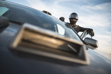 Rally car driver concept. A man in the helmet is standing near the car outdoors.