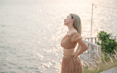 Asian woman wearing dress posing on the beach, golden sea sunset moment.