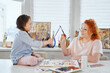 © boytsov - Happy family hobby-time together: mother and daughter painting together in art studio using paint brushes and acrylic paint or watercolor. Woman helping or teaching daughter sitting on a table to draw