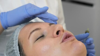 Wall Mural - Cosmetologist is applying yellow peeling on woman's face massaging movements in beauty clinic. Beautician is making cure procedure on patient's face, closeup view.