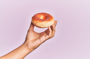 Wall Mural - Hand of hispanic man holding donut over isolated pink background.