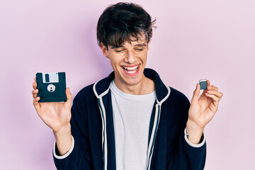 Poster - Handsome hipster young man holding floppy disk and sdxc card smiling and laughing hard out loud because funny crazy joke.