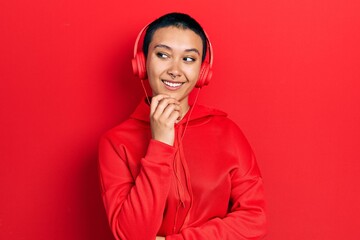 Canvas Print - Beautiful hispanic woman with short hair listening to music using headphones with hand on chin thinking about question, pensive expression. smiling with thoughtful face. doubt concept.