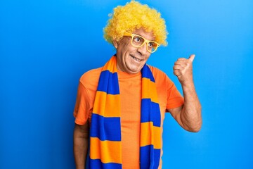 Wall Mural - Senior hispanic man football hooligan cheering game pointing thumb up to the side smiling happy with open mouth