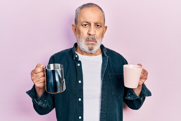 Poster - Handsome senior man with beard holding coffee and milk relaxed with serious expression on face. simple and natural looking at the camera.