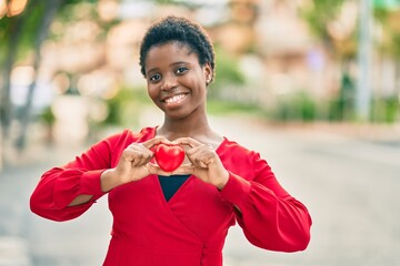 Poster - Young african american woman smiling happy holding heart standing at the city.