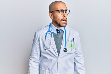 Poster - Hispanic adult man wearing doctor uniform and stethoscope angry and mad screaming frustrated and furious, shouting with anger. rage and aggressive concept.