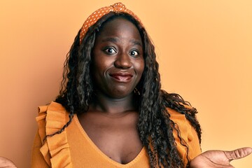 Poster - African young woman wearing casual clothes over yellow background clueless and confused expression with arms and hands raised. doubt concept.