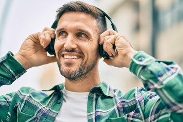 Wall Mural - Young caucasian man smiling happy using headphones at the city.