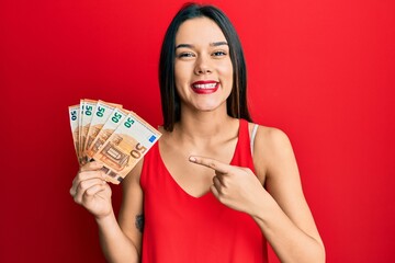 Wall Mural - Young hispanic girl holding euro banknotes smiling happy pointing with hand and finger