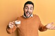 © Krakenimages.com - Young hispanic man holding coffee celebrating achievement with happy smile and winner expression with raised hand