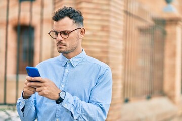 Poster - Young hispanic businessman with serious expression using smartphone at the city.