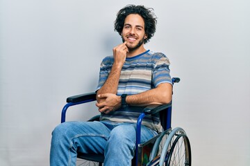 Sticker - Handsome hispanic man sitting on wheelchair looking confident at the camera smiling with crossed arms and hand raised on chin. thinking positive.