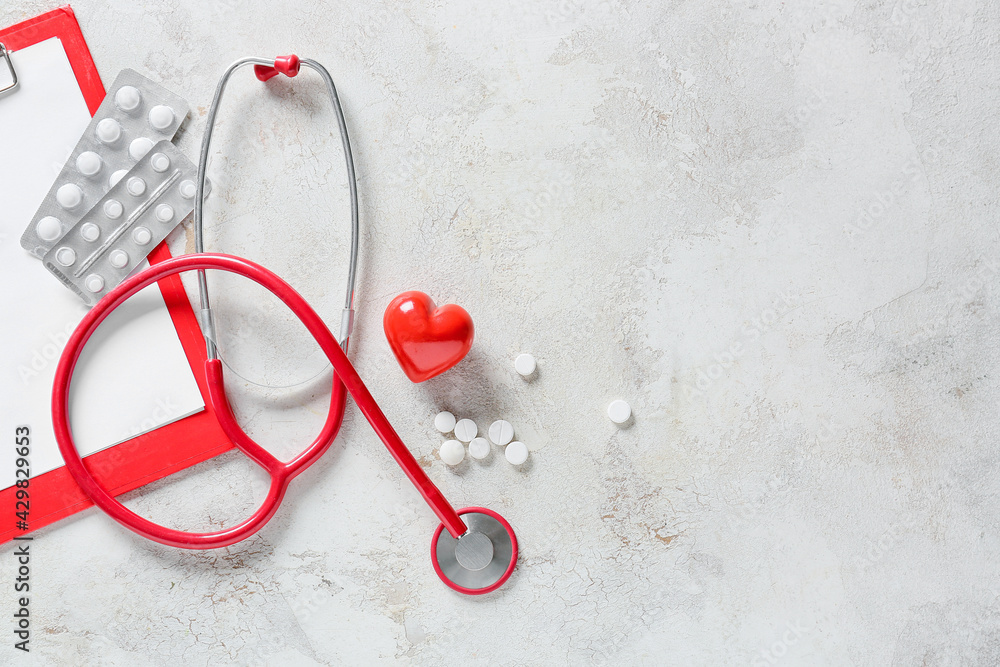Modern stethoscope, pills and heart on light background