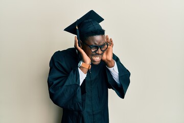 Wall Mural - Handsome black man wearing graduation cap and ceremony robe trying to hear both hands on ear gesture, curious for gossip. hearing problem, deaf