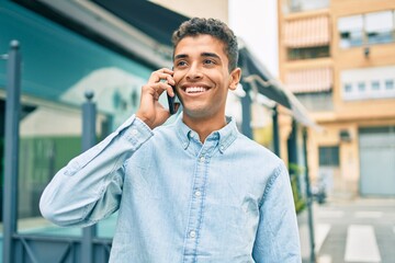 Poster - Young latin man smiling happy talking on the smartphone walking at the city.