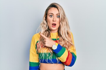 Canvas Print - Beautiful young blonde woman wearing colored sweater surprised pointing with finger to the side, open mouth amazed expression.