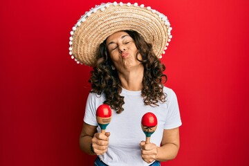 Wall Mural - Middle age hispanic woman holding mexican hat playing maracas looking at the camera blowing a kiss being lovely and sexy. love expression.