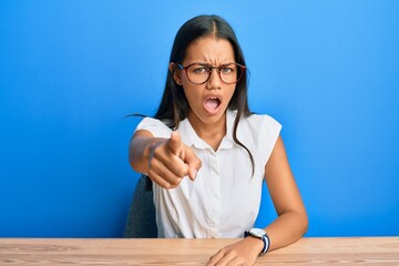 Wall Mural - Beautiful hispanic woman wearing casual clothes sitting on the table pointing displeased and frustrated to the camera, angry and furious with you