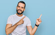 © Krakenimages.com - Young man with beard wearing casual white t shirt smiling and looking at the camera pointing with two hands and fingers to the side.