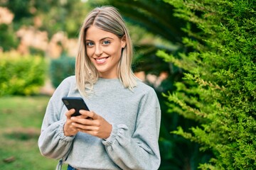 Young blonde girl smiling happy using smartphone at the park.