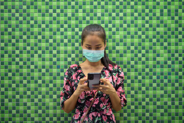 Wall Mural - Portrait of woman wearing face mask for protection against coronavirus Covid-19 at night against colorful wall with copy space while texting with mobile phone