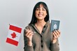 © Krakenimages.com - Young hispanic woman holding canada flag and passport smiling with a happy and cool smile on face. showing teeth.