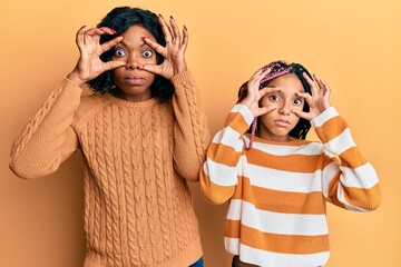 Wall Mural - Beautiful african american mother and daughter wearing wool winter sweater trying to open eyes with fingers, sleepy and tired for morning fatigue