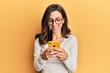 © Krakenimages.com - Young brunette woman using smartphone over yellow background smiling with a happy and cool smile on face. showing teeth.