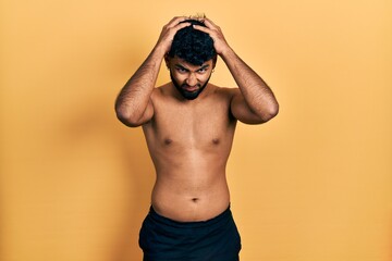 Canvas Print - Arab man with beard wearing swimwear shirtless suffering from headache desperate and stressed because pain and migraine. hands on head.