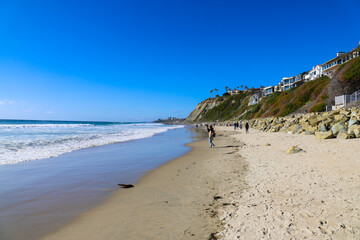 people walking along the beach on silky sand near vast blue ocean water with waves rolling in and blue sky at Dana Strands Beach in Dana Point, California