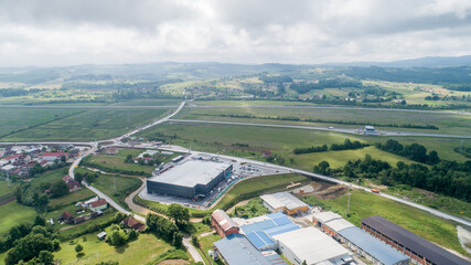 Wall Mural - Aerial view of traffic roads amid green fields with trees and buildings under a cloudy sky