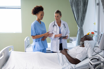 Wall Mural - Two diverse female doctors and african american male patient in hospital room talking