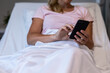 © wavebreak3 - Midsection of caucasian female patient lying on hospital bed using smartphone
