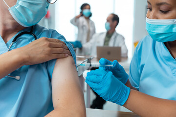 Wall Mural - African american female doctor giving covid vaccination to male colleague, both in face masks