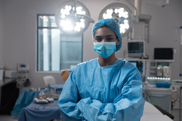 Wall Mural - Mixed race female surgeon with face mask wearing protective clothing in operating theatre