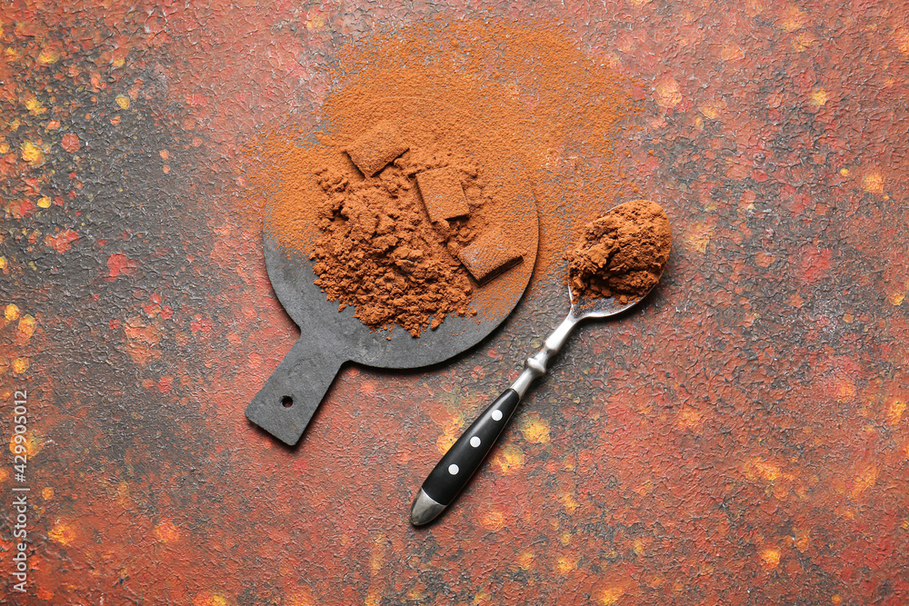 Spoon and board with cocoa powder on grunge background