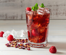 Cold Sparkling Hibiscus Or Karkade Ice Tea With Lemon, Mint, And Raspberry In Glass On A Wooden Table. Healthy Drink.
