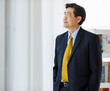 Portrait shot of Asian senior old successful company entrepreneur in formal suit with brown necktie and golden eyeglasses standing against white background