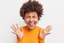 Joyful Afro American Woman Expresses Happiness Smiles Broadly Keeps Eyes Closed Raises Palms Has Upbeat Mood Sends Positive Vibes Dressed Casually Isolated Over White Background. Emotions Concept