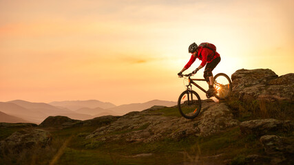 Cyclist in Red Riding Bike on the Summer Rocky Trail at Sunset. Extreme Sport and Enduro Biking Concept.